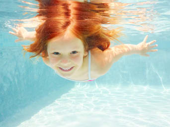 Sicurezza in piscina: una bambina nuota sott’acqua in una piscina.