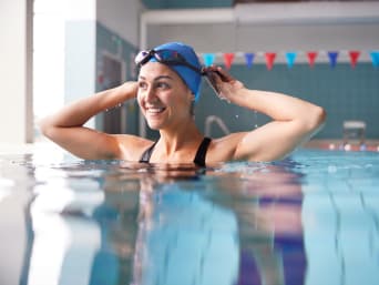 Beneficios de la natación para la salud: una nadadora se coloca las gafas en una piscina cubierta.