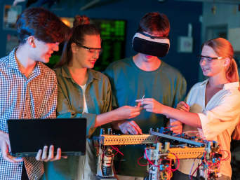 Czworo nastolatków pracuje wspólnie nad projektem w laboratorium robotycznym.