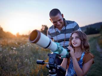 Astronomia per bambini: papà e figlia guardano il cielo con un telescopio.
