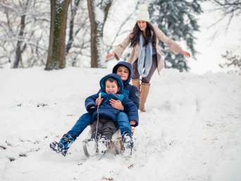 Winterurlaub Bayerischer Wald mit Kindern – Mutter und Kinder am Rodelhang.