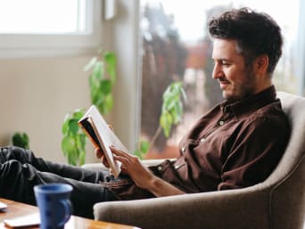 Ideas de autocuidado diario: un hombre lee tranquilamente un libro en casa.