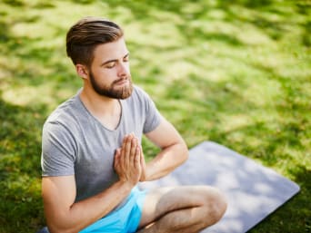 Beneficios de la meditación: un hombre medita sentado en una esterilla de yoga sobre el césped de un parque.