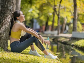 Sport na stres: kobieta uprawiająca jogging robi przerwę i opiera się o pień drzewa. 
