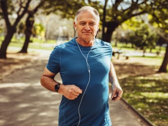 Sporten tegen stress: oudere man jogt op een straat met bomen. 