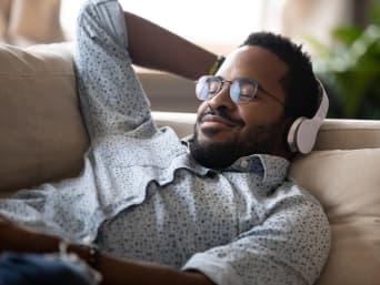 Relax a casa: uomo disteso sul divano ascolta un audiolibro.