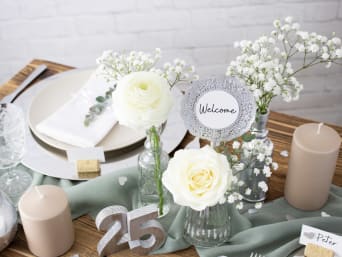 Zilveren bruiloft decoraties: Gedekte tafel met bloemen en een zilveren 25-jarig huwelijksjubileum.