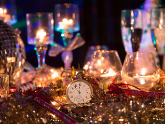 Elementos decorativos dorados y brillantes y copas de cava en una mesa de Nochevieja.