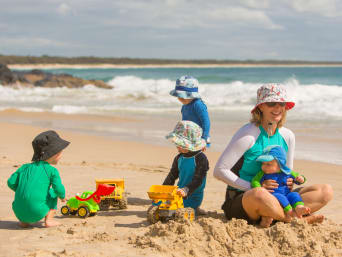 Ochrana dětí před sluncem: Batolata na pláži v oblečení chránícím před UV zářením.