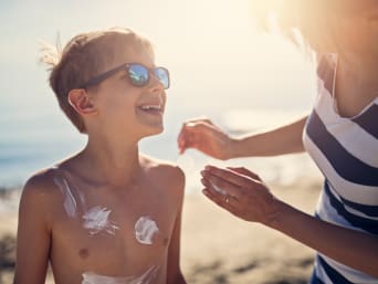 Protección solar para niños: una madre pone crema solar a su hijo en la playa.