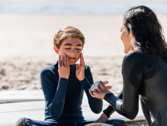 Zonnebrandcrème tijdens sporten: moeder en zoon smeren zich in voor het surfen.