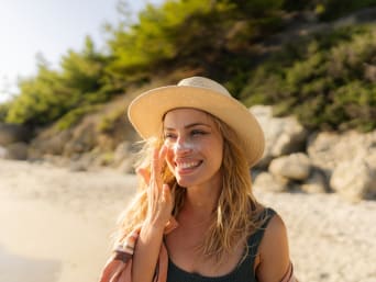 Cremas de protección solar: una mujer joven se pone crema solar en la playa. 