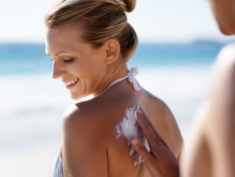 Cremas de protección solar: una mujer es untada con crema solar por su acompañante en la playa.