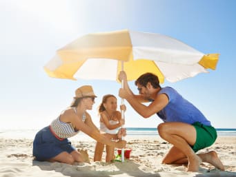 Protezione solare confronto: famiglia in spiaggia apre l’ombrellone per proteggersi dal sole in spiaggia.