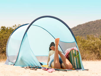 Ochrona skóry przed promieniowaniem UV i wiatrem: kobieta leży pod namiotem plażowym.
