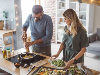 Hábitos de vida sostenibles: una pareja cocina un plato vegetariano con verduras y hortalizas de temporada.