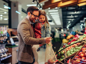 Consumo responsable y sostenible: un padre y su hija compran fruta en un supermercado.