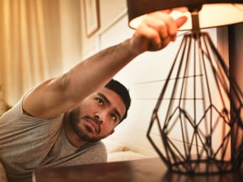 Comment réduire sa consommation électrique : un homme éteint sa lampe de chevet.