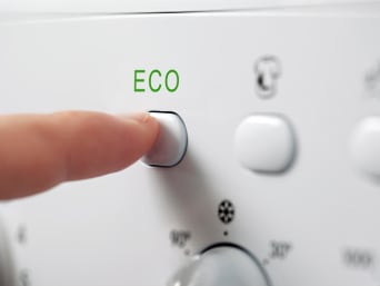 Stromverbrauch senken – Eine Person drückt das Eco-Programm an der Waschmaschine.