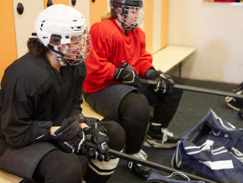 Eishockey Ausrüstung: Zwei Spielerinnen sitzen in ihrer Eishockey-Ausrüstung in der Umkleide.