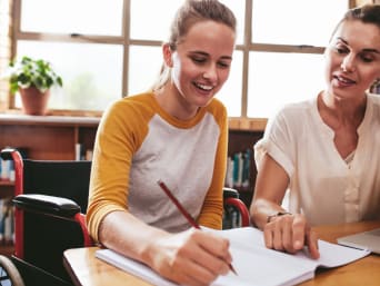 Studenti con BES: studentessa su sedia a rotelle studia insieme a un’assistente.