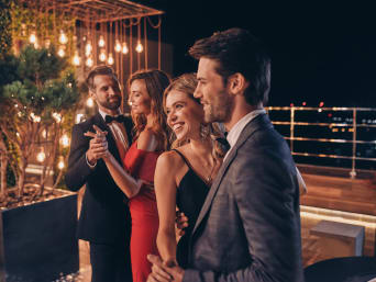Zwei junge Paare in Kleid und Anzug tanzen auf der Terrasse.