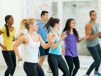 Grupa w sali fitness wykonuje dance cardio – trening taneczny poprawiający wydolność organizmu.