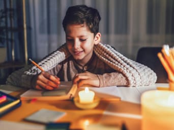 Hoe elektriciteit te besparen met kinderen - jongen maakt zijn huiswerk bij kaarslicht.