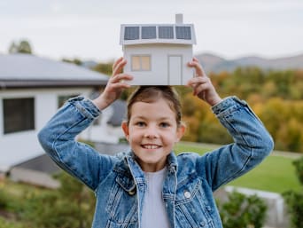 Hernieuwbare energie uitgelegd aan kinderen - meisje met een model van een huis met zonnepanelen.