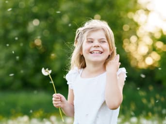 Umweltbewusstsein – kleines Mädchen freut sich über eine Pusteblume auf der Wiese.