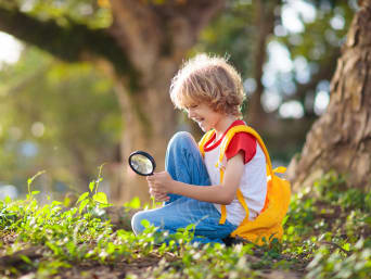 Milieueducatie: kleine jonge onderzoekt planten met een vergrootglas.