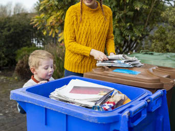 Separare i rifiuti: un bambino guarda all’interno del cassonetto della carta.