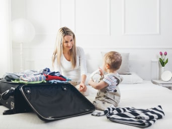 Inpaklijst vakantie – klein kind kijkt toe hoe mama een koffer inpakt.