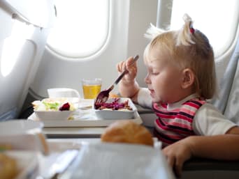 Consejos para viajar en avión con niños: una niña pequeña come en un avión.