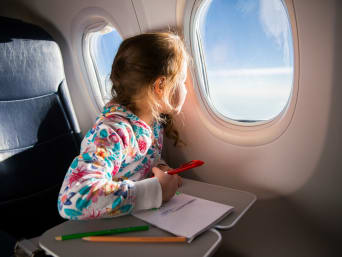 Volar en avión con niños: una niña pequeña mira por la ventana del avión.