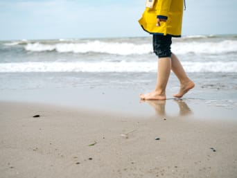 Familienurlaub Ostsee: Kind in gelber Regenjacke läuft barfuß am Strand entlang.