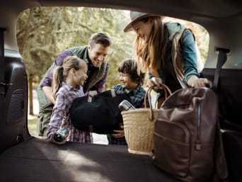 Packliste Familienurlaub – Familie holt das Gepäck aus dem Auto.