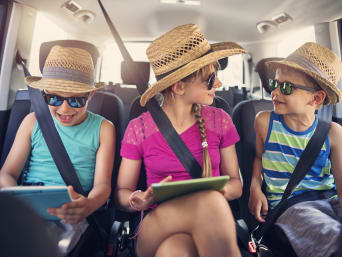 Activités en voiture : 3 enfants jouent sur leur tablette en voiture.
