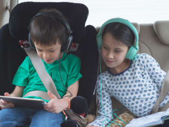 Spiele im Auto: Kinder nutzen im Auto ein Tablet und Kopfhörer.
