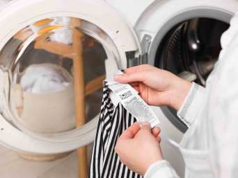 Katoen wassen: vrouw bekijkt het waslabel in een katoenen kledingstuk. Katoen wassen: vrouw bekijkt het waslabel in een katoenen kledingstuk.