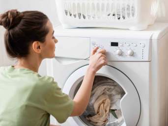 Polyester waschen: Frau stellt das richtige Waschmaschinenprogramm für synthetische Wäsche ein. Polyester waschen: Frau stellt das richtige Waschmaschinenprogramm für synthetische Wäsche ein.