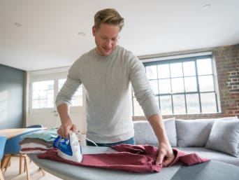 A man ironing a shirt on an ironing board.