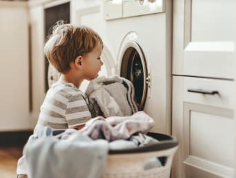 Significado de los símbolos de las etiquetas de lavado: un niño mete ropa en la lavadora.