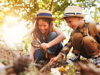Experimentos en el bosque para niños: dos niños exploran el suelo del bosque con una lupa.