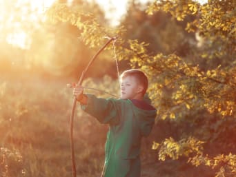 Attività nel bosco per bambini – Ragazzino si esercita con l’arco in un bosco.