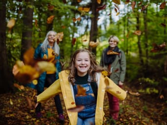 Paseo por el bosque con niños: una niña lanza hojas de árbol al aire.