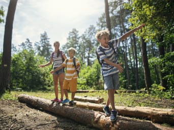 Giochi nel bosco – Alcuni bambini cercano di stare in equilibrio su un tronco a terra.