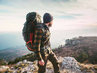 Wyposażenie turysty pieszego: podróżnik podczas trekkingu z plecakiem spogląda w dal.