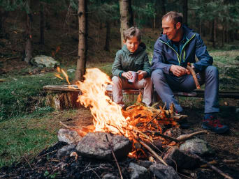 Vater und Sohn machen ein Lagerfeuer an einer Feuerstelle.