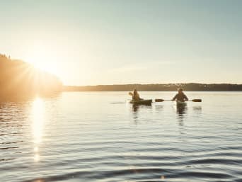 Kanufahren: Pärchen in 1er-Kajaks fährt im Sonnenschein auf einem See.